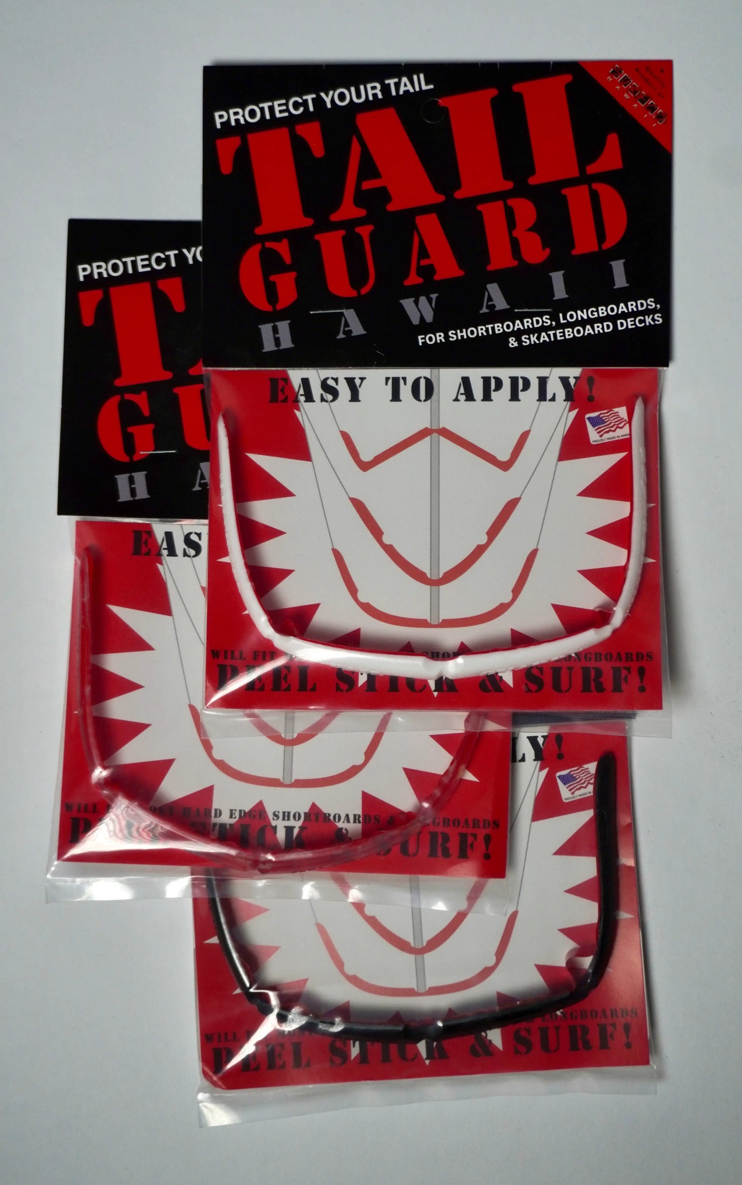 Balení SurfCo Hawaii Tail Guard Kit – různé barevné varianty (černá, průhledná, bílá) v originálním obalu, peel-stick instalace.