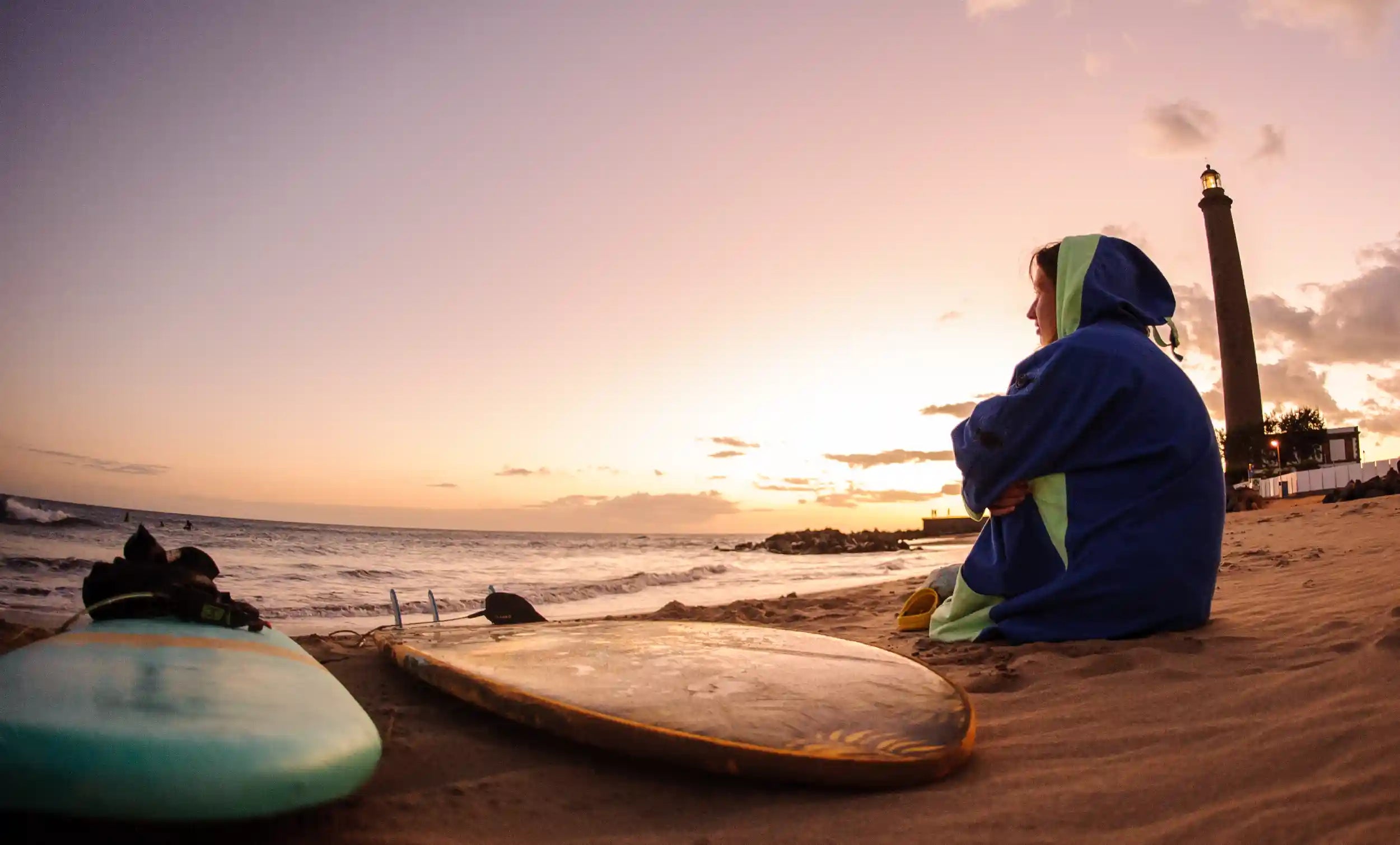dívka sedí na pláži v ponchu surfboard, zapadající slunce, sunset