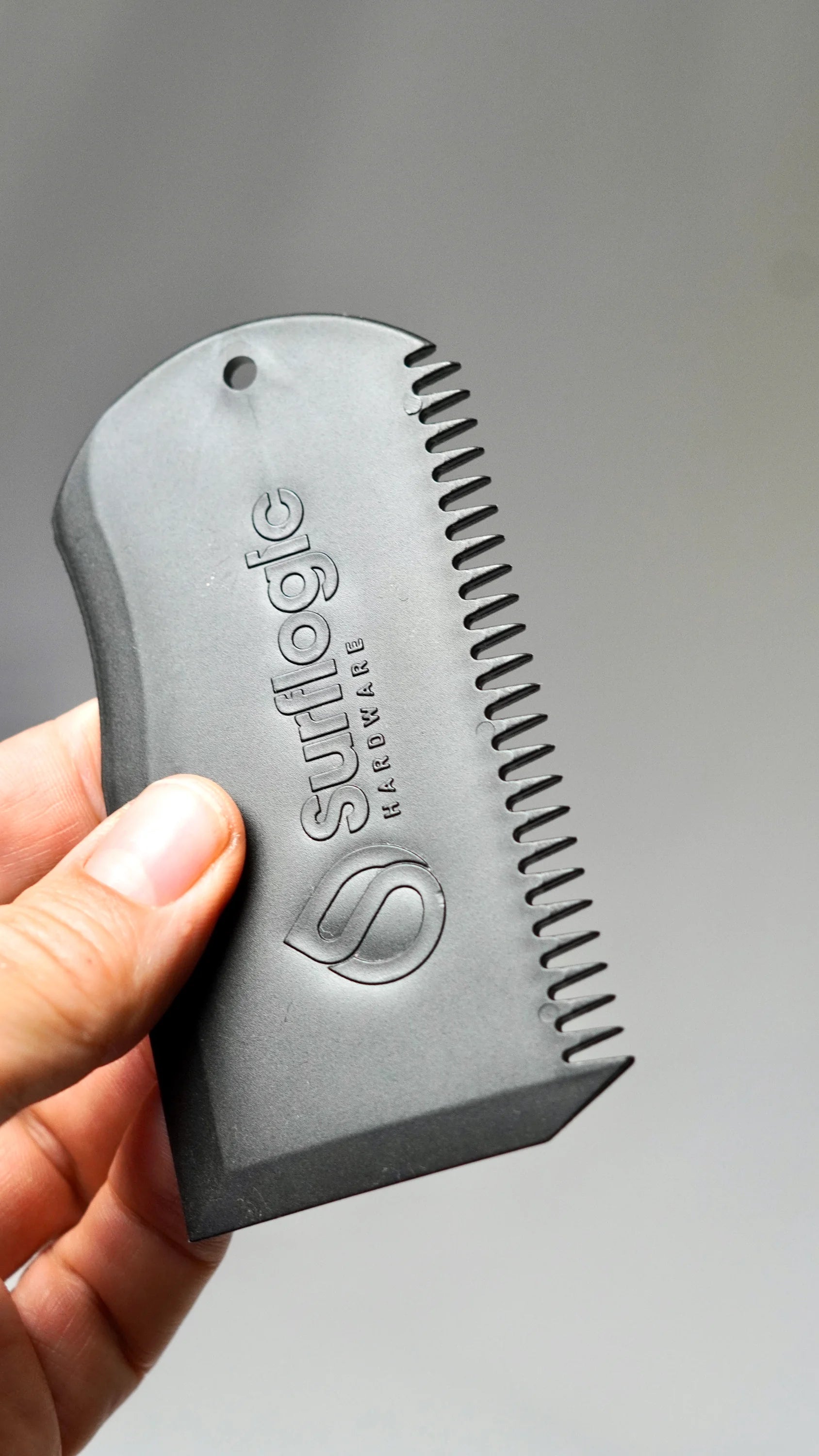 černý Surflogic Wax Comb v ruce – škrabka a hřeben na surfový vosk