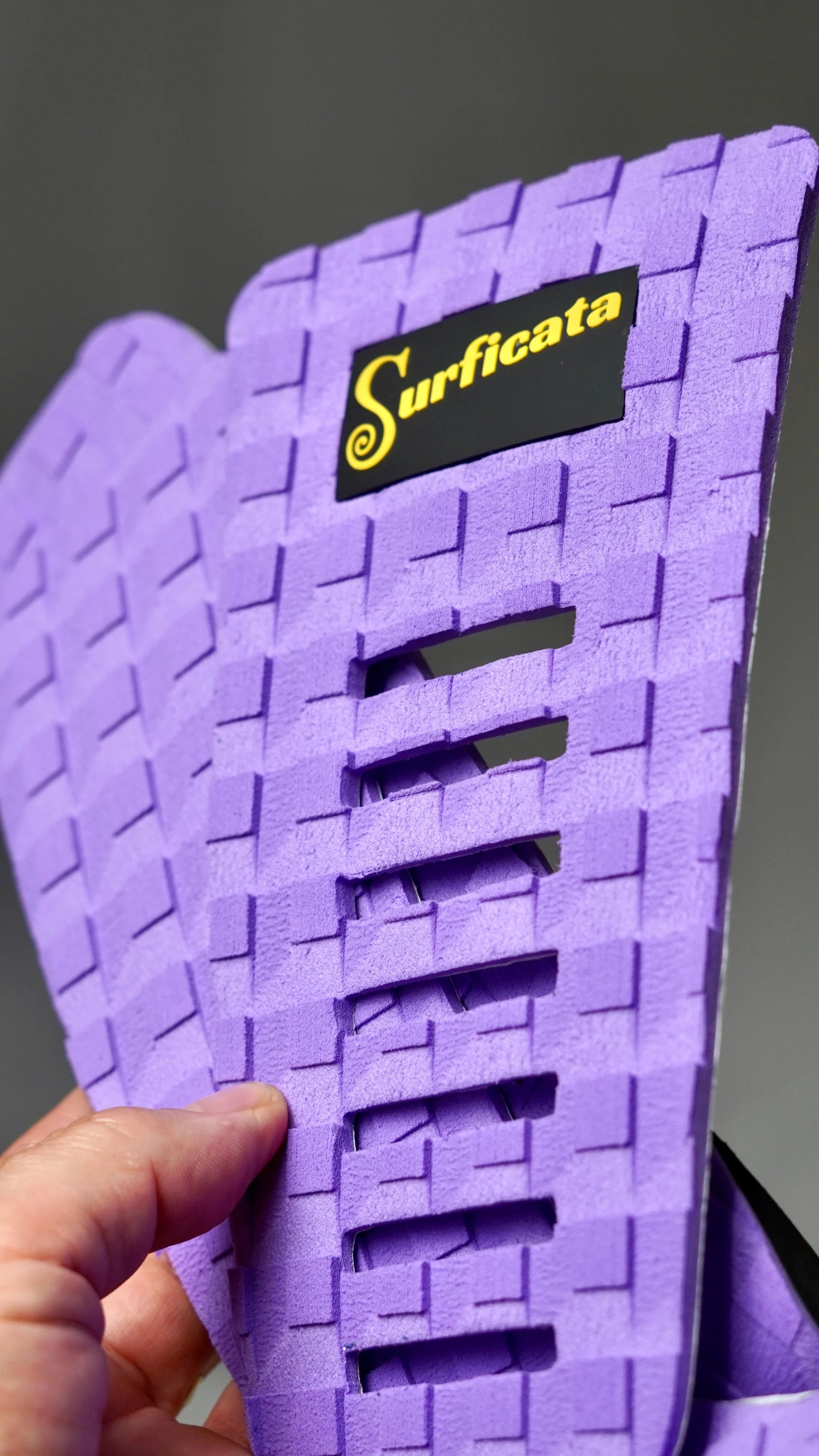 Fialový tail pad Surficata Purple Haze držený v ruce, detail EVA struktury a podélných výřezů.